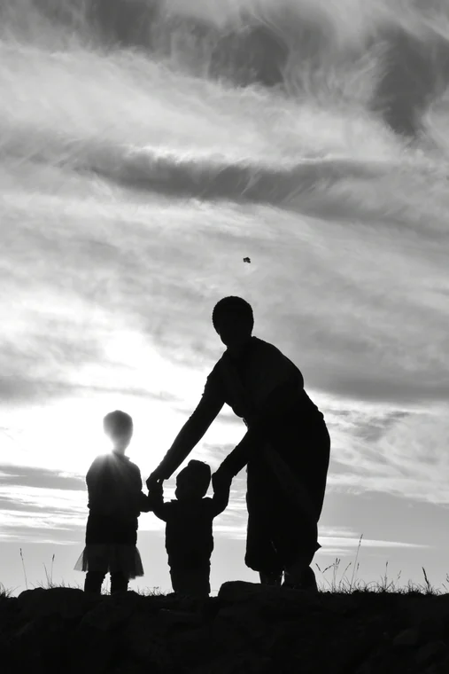 Eine erwachsene Person und zwei Kinder als Silhouetten unter einem weiten Himmel.